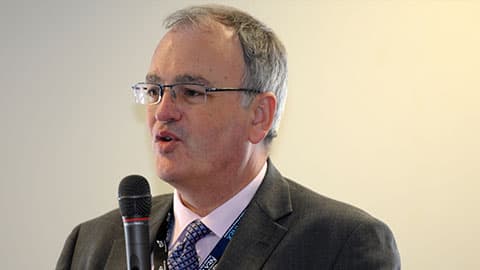 A close up of Richard wearing a suit and speaking into a microphone.